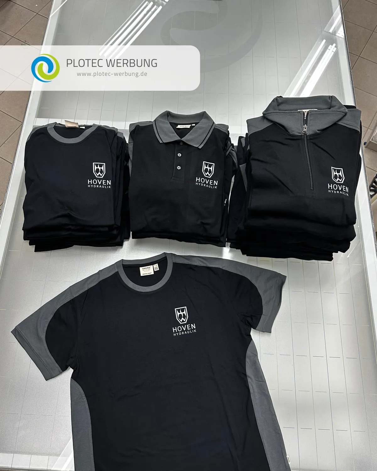 Gestapelte schwarz-graue Arbeitskleidung mit dem Logo von Hoven Hydraulik