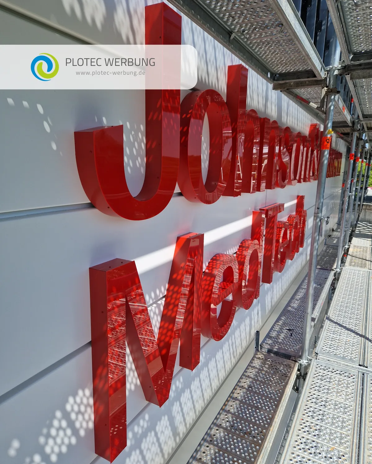 Rote Profilbuchstaben Johnson MedTech an einer hellen Fassade, fotografiert vom Montagegerüst