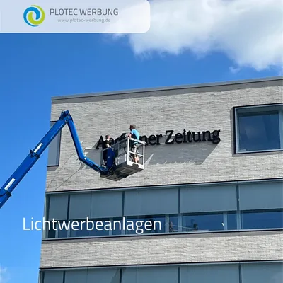 Monteur im Hubsteiger bringt den Schriftzug Aachener Zeitung an einer hellen Fassade an