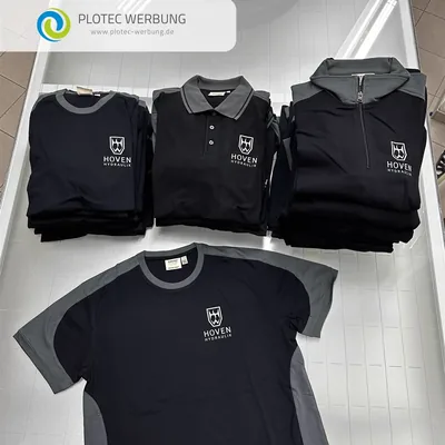 Gestapelte schwarze T-Shirts, Poloshirts und Zip-Sweatshirts mit besticktem Firmenlogo
